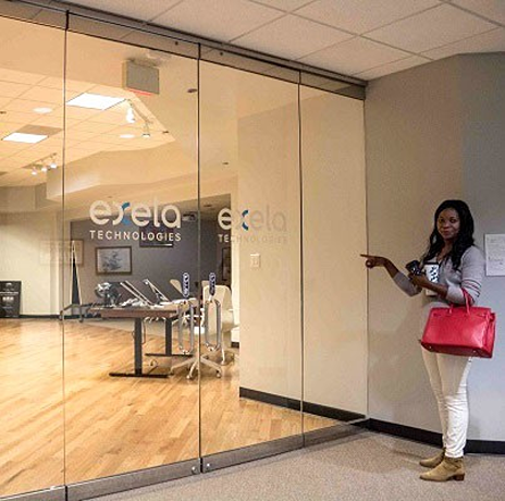 Ebbah pointing toward a glass-walled office space labeled Exela Technologies.
