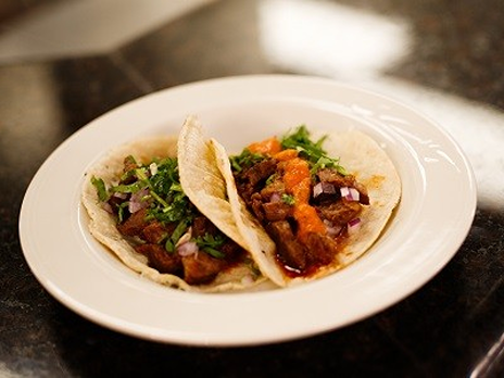 Tacos al pastor served on corn tortillas. The food is served on a plate on a marble table.