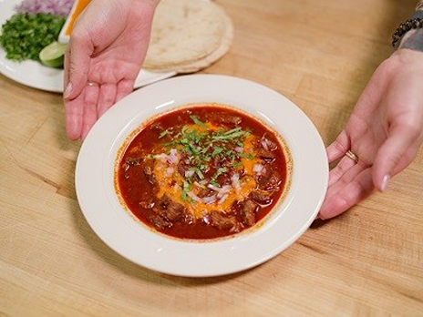 Hutchinson holds a bowl of Sopa Azteca with cilantro tortillas behind it on a table in a Dallas College kitchen.