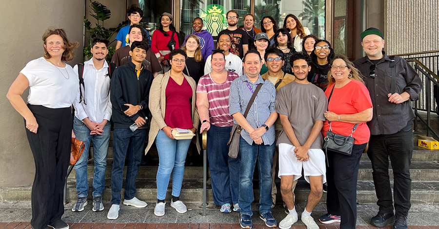 20 students and 4 advisors stand n steps in front of a Starbucks logo on a glass window in New Orleans.
