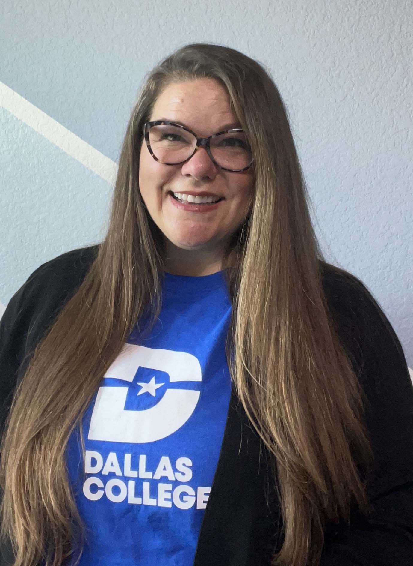 Dr. Meagan Pollock in a blue Dallas College shirt sits at a desk.