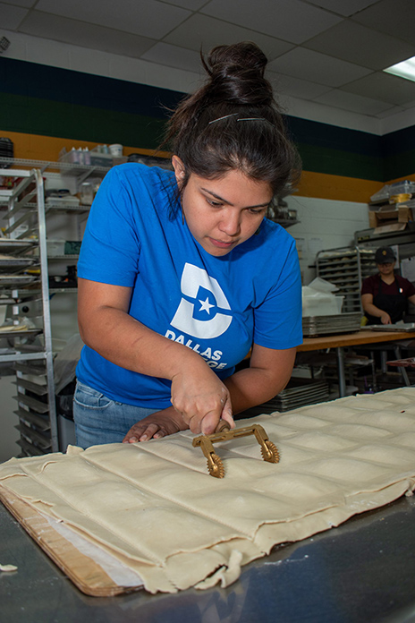 Maricsa cutting tarts in a Dallas College shirt in La Casita Bakeshop.