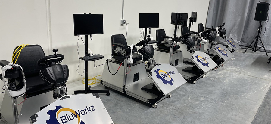 A row of 5 forklift simulators that are metal with the Blu-Workz logo on the outside. The simulator has a car steering wheel like set up that is black.