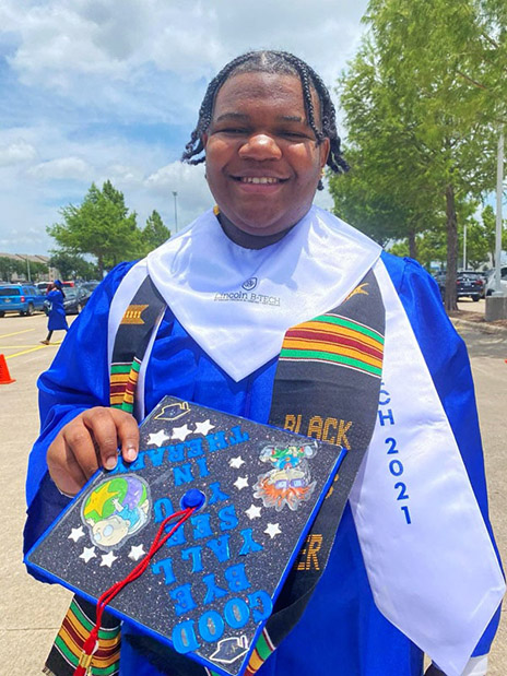 Graduation portrait of Elijah Harrington outdoors in a blue cap and gown, holding a decorated graduation cap and wearing multiple honor stoles and cords.