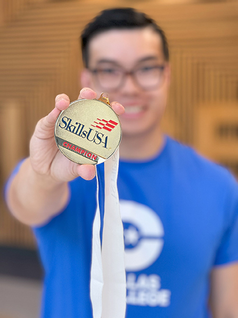 A close-up photograph of Dallas College student Harrison Nguyen smiling confidently while holding his medal in his hand and showing it to the camera.