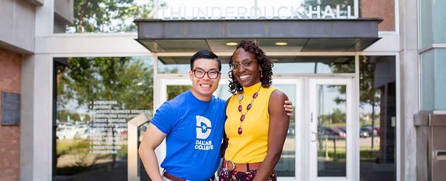Harrison, a Dallas College student, and Accessibility Services staff member stand together outside of a building on a Dallas College campus, smiling at the camera