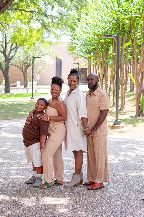 Kirsten and her family in brown and white stand on a walkway lined with trees.