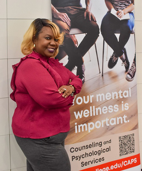 Nykesha stands beside a Counseling and Psychological Services (CAPS) banner that promotes mental wellness resources for students. The banner features the message 