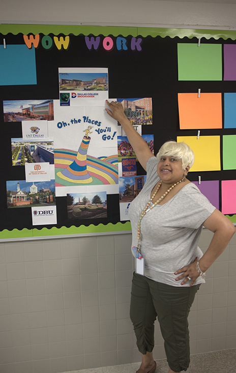 Teacher Raven Furlough pointing to a bulletin board with the words 