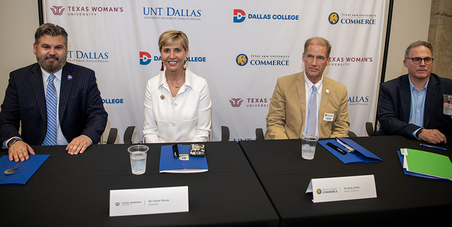 Chancellor Lonon and representatives from the other universities sit at a signing table in front of a backdrop with the universities logo.
