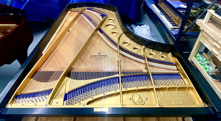 The top of the piano is removed, showing the golden interior of the piano with the strings and tuning pins inside Soto's workshop. The piano has a C. Bechstein branding inside.
