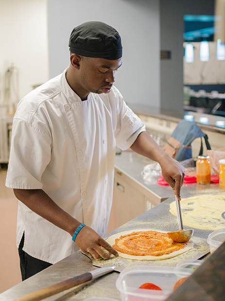 Tairan Lockett putting sauce on a pizza.