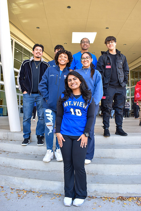 Tiffiya, wearing a blue Mountain View jersey, stands on a set of stairs with her SGA friends. They also smile towards the camera in front of a building on a Dallas College campus.