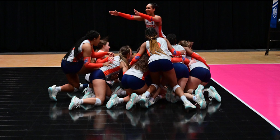 Volleyball team celebrating by piling on top of each other on the floor.