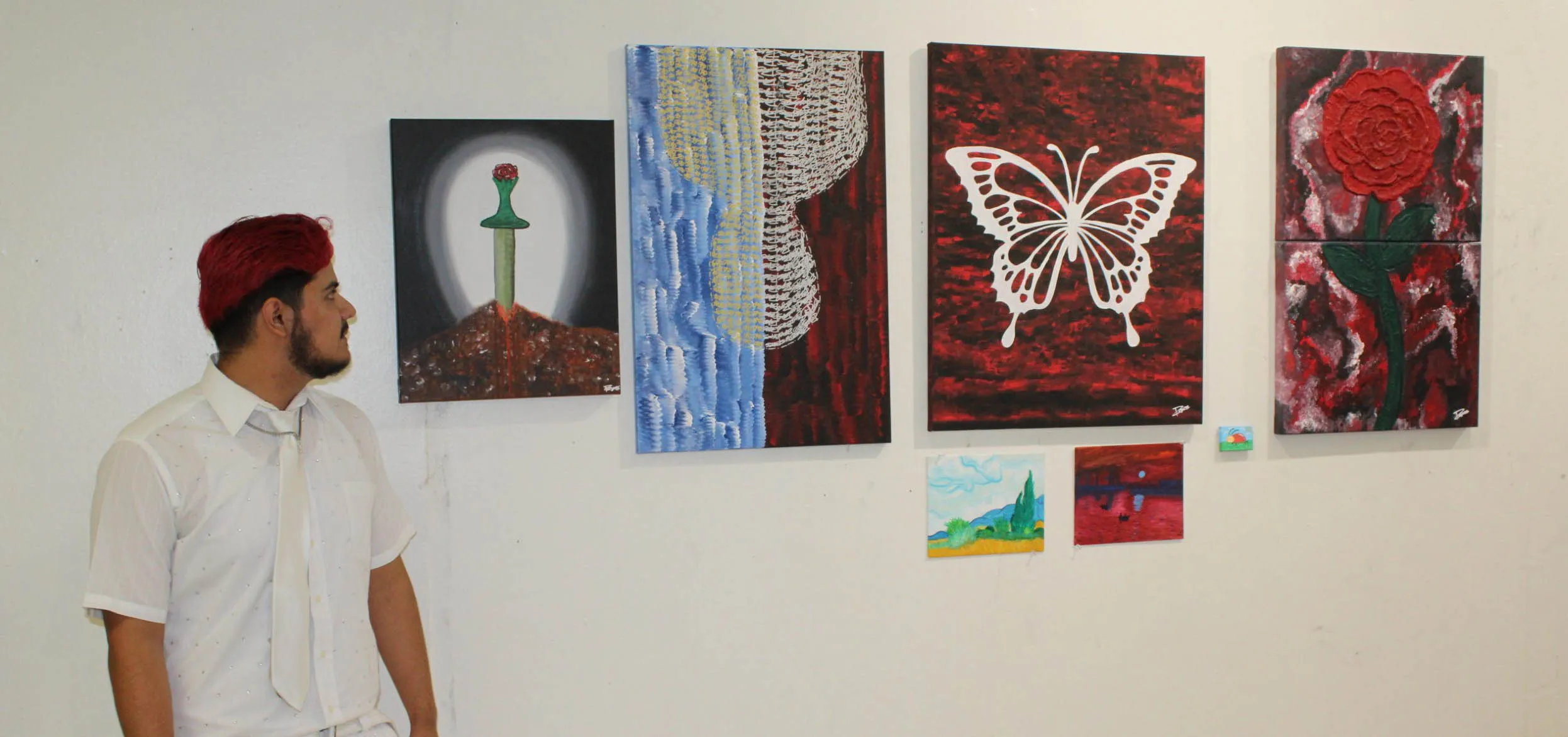 Osvaldo looking at all of his art on the wall from the side while standing.