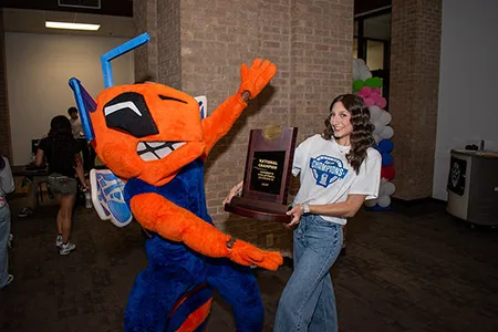 Mia Santos holding trophy out to Harvester Bee mascot.