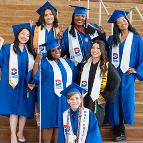 The seven 2025 graduation speakers pose for a photo on a set of stairs, wearing their regalia
