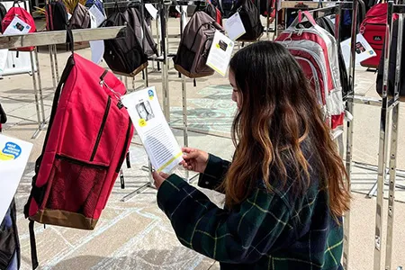 A student stands in front of a backpack reading a story as part of the Send Silence Packing exhibit.