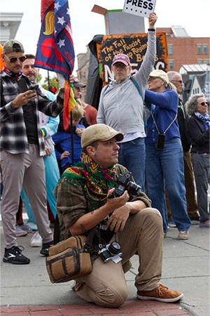 A student journalist is seen holding a camera in a crowd of people.