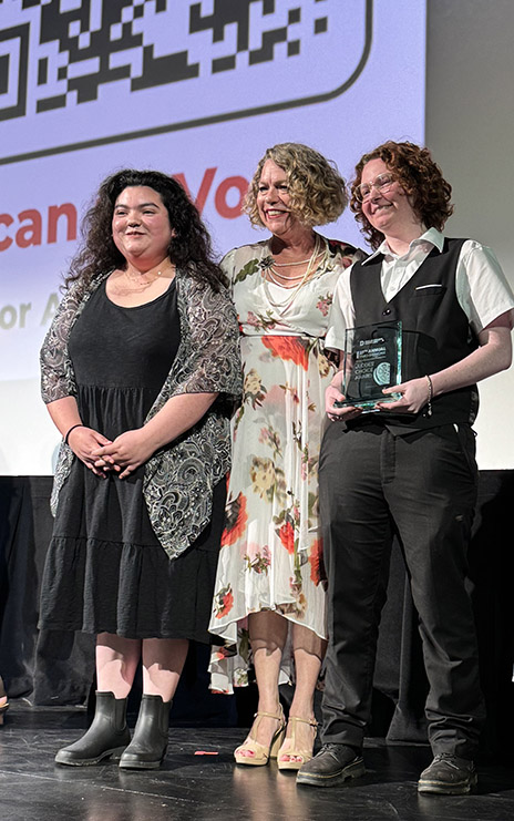 Melany Zarate, Sharie Vance and Sun Burns standing on stage with trophy.