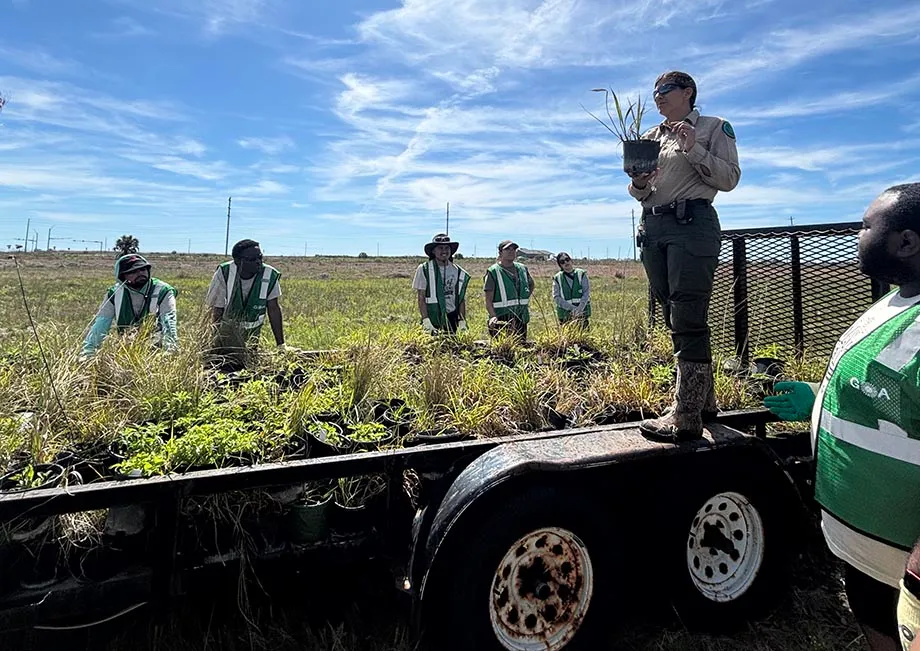 Person standing on truck give instruction to students standing in the field.