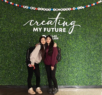 Two students posing in front of Instagram wall with oversized 60th anniversary friendship bracelet.