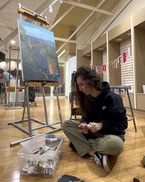 Khugayeva sitting on the floor sorting through her paints.