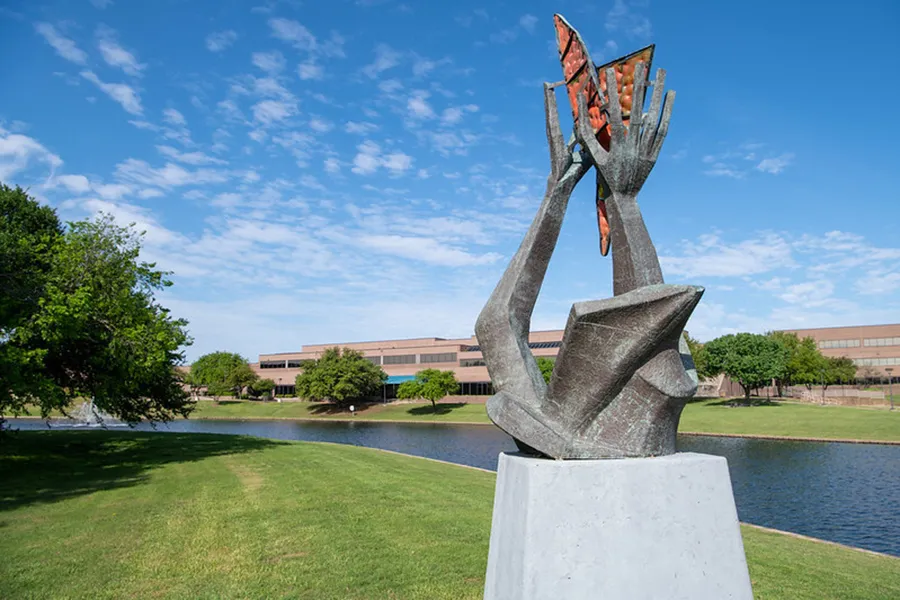 Sculpture with two hands holding a butterfly on the shore of pond.
