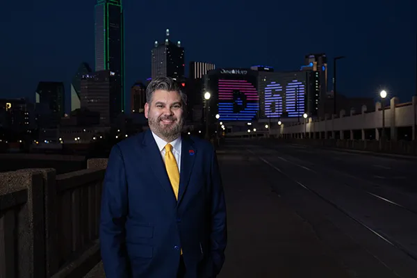 Dallas College Chancellor Justin Lonon stands with the downtown skyline, featuring the Dallas College logo, behind him.