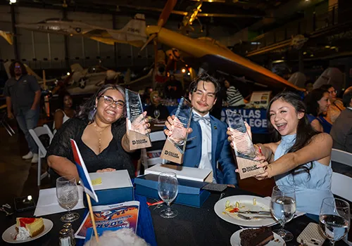 Three students seated at a table show off their awards at the Student Leadership Awards and Sneaker Ball event.