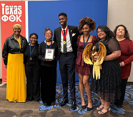 Seven PTK students standing in front of a Texas OK backdrop.