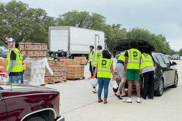 Volunteers wearing bright yellow vests help load food into cars