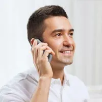 A smiling man in a white shirt holds a phone to his ear, appearing engaged in a pleasant conversation