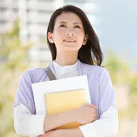 A woman with long dark hair holds a notebook, looking upward with a hopeful expression