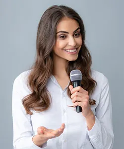 Smiling student communicating with long brown hair holding a microphone, dressed in a white shirt