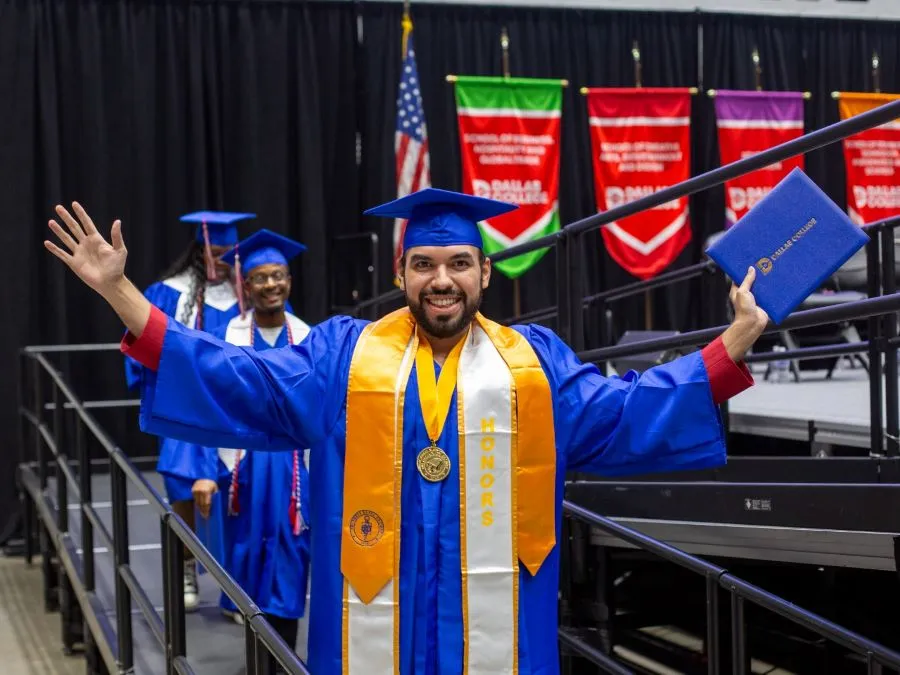 A PTK student walks off the stage at graduation with his arms outstretched, holding his diploma in his hand.