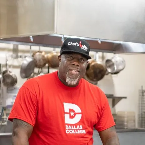 A student with a Dallas College shirt stands in a commercial kitchen